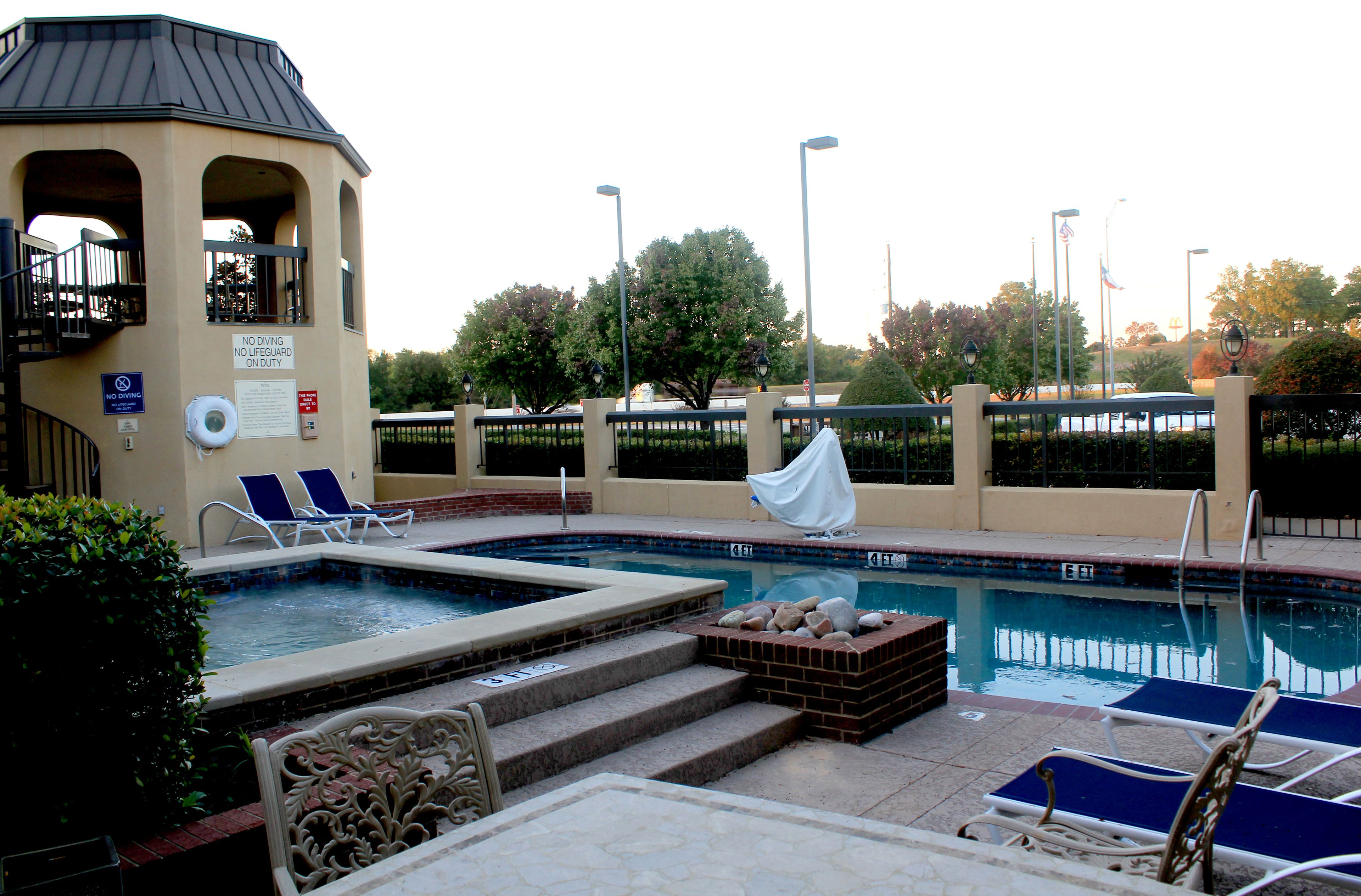 Una piscina con sillones de descanso, una torre de socorristas y una zona techada.