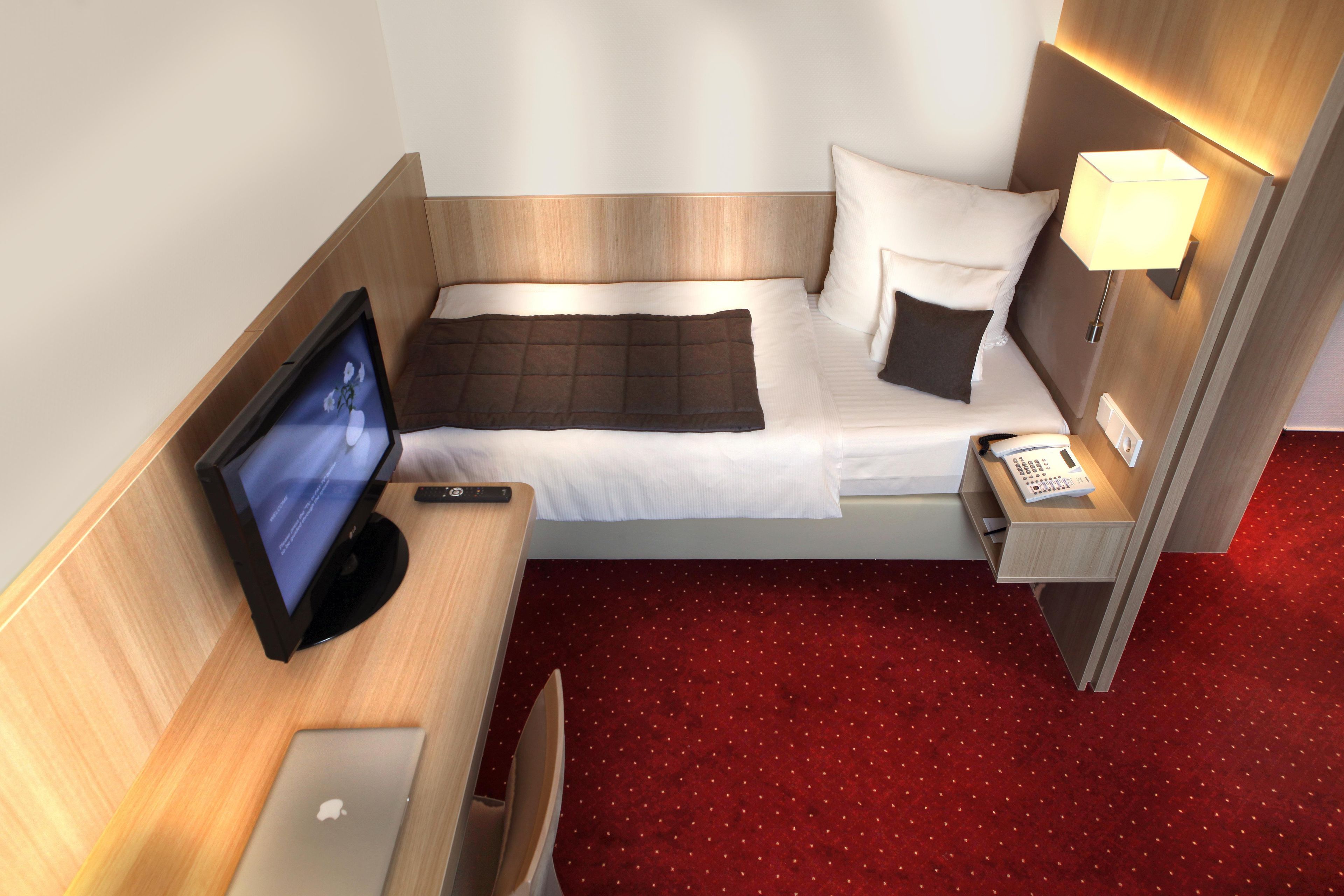 Ein Hotelzimmer mit einem Bett, einem Schreibtisch mit Computer, einem Fernseher, einem Telefon und einer Lampe.