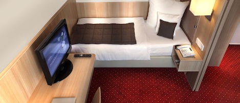 A hotel room with a bed, a desk with a computer, a TV, a phone, and a lamp.