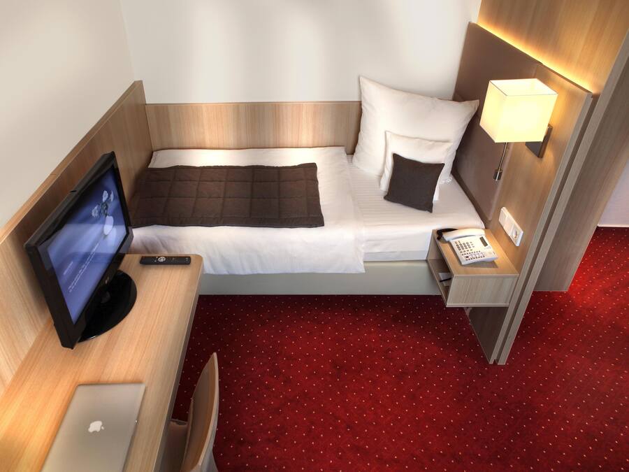 Habitación de hotel con cama, escritorio, computadora, televisor, teléfono y lámpara.
