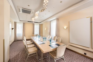 Una sala conferenze con un lungo tavolo, sedie, una lavagna e un tappeto decorato.