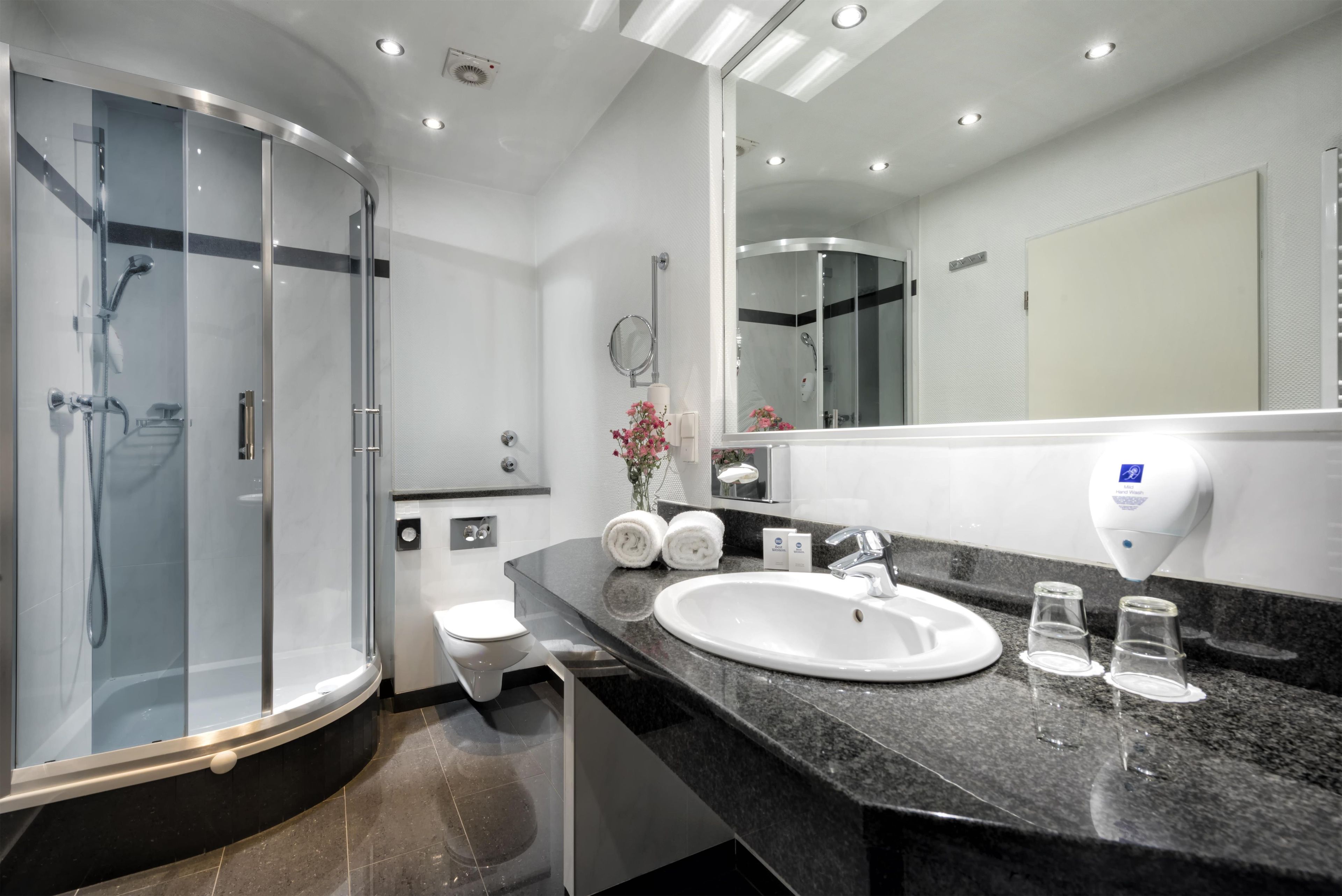 Ein modernes Badezimmer mit einer begehbaren Glasdusche, einem weißen Waschbecken und einem großen Spiegel.