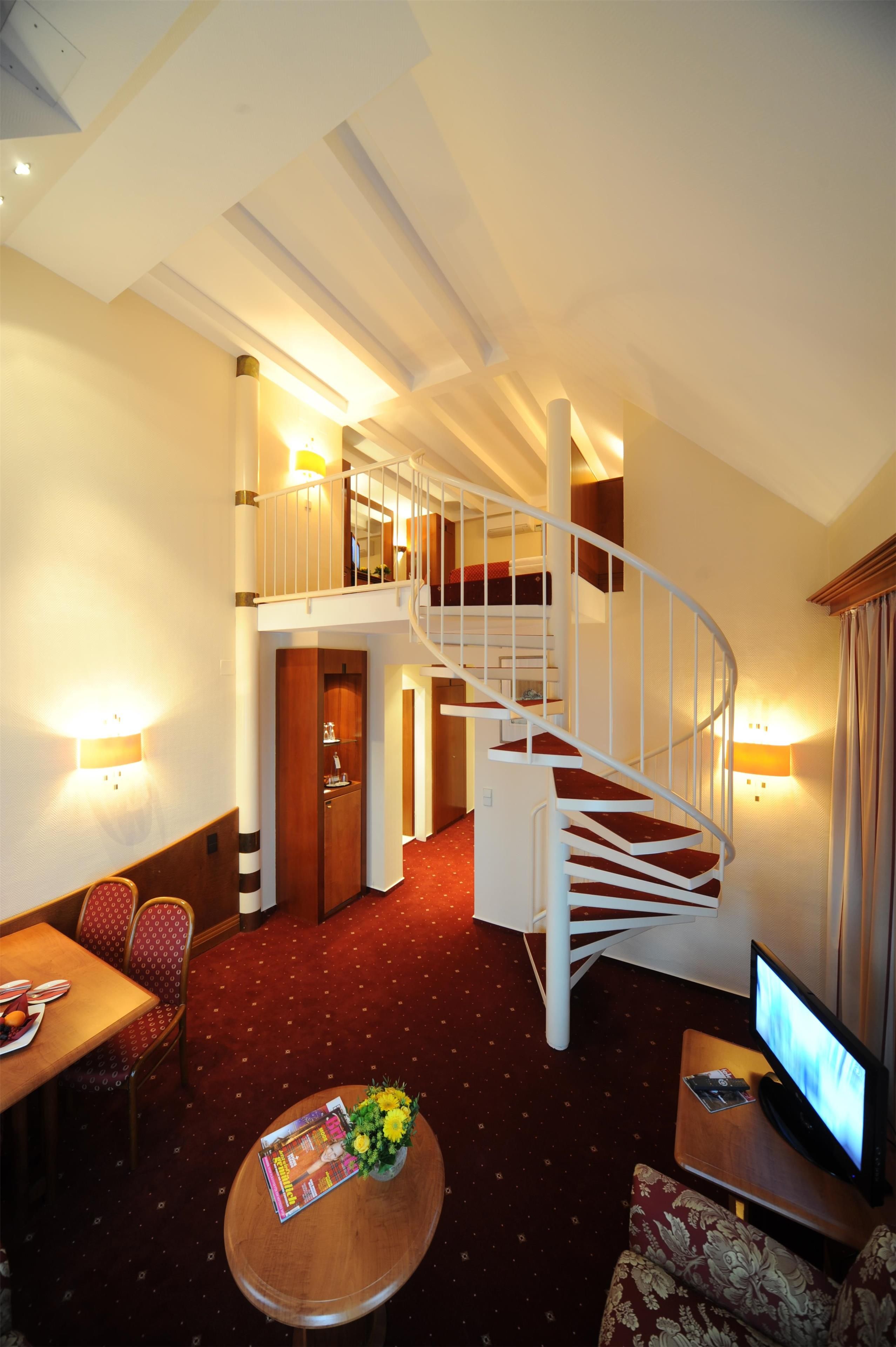 Ein Hotelzimmer mit rotem Teppich, einem Holztisch, einer Couch, einem Fernseher und einer Treppe.