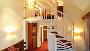 A hotel room with a red carpet, a wooden dining table, a sofa, a TV, and a staircase.