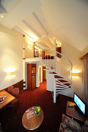 A hotel room with a red carpet, a wooden dining table, a sofa, a TV, and a staircase. - Best Western Hotel Zur Post (Bremen)