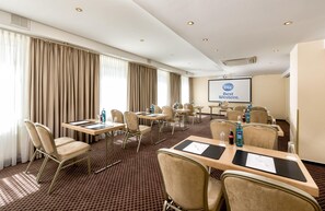 Een vergaderruimte met tafels, stoelen, een projectiescherm waarop 'Best Western' staat en een groot raam met gordijnen.