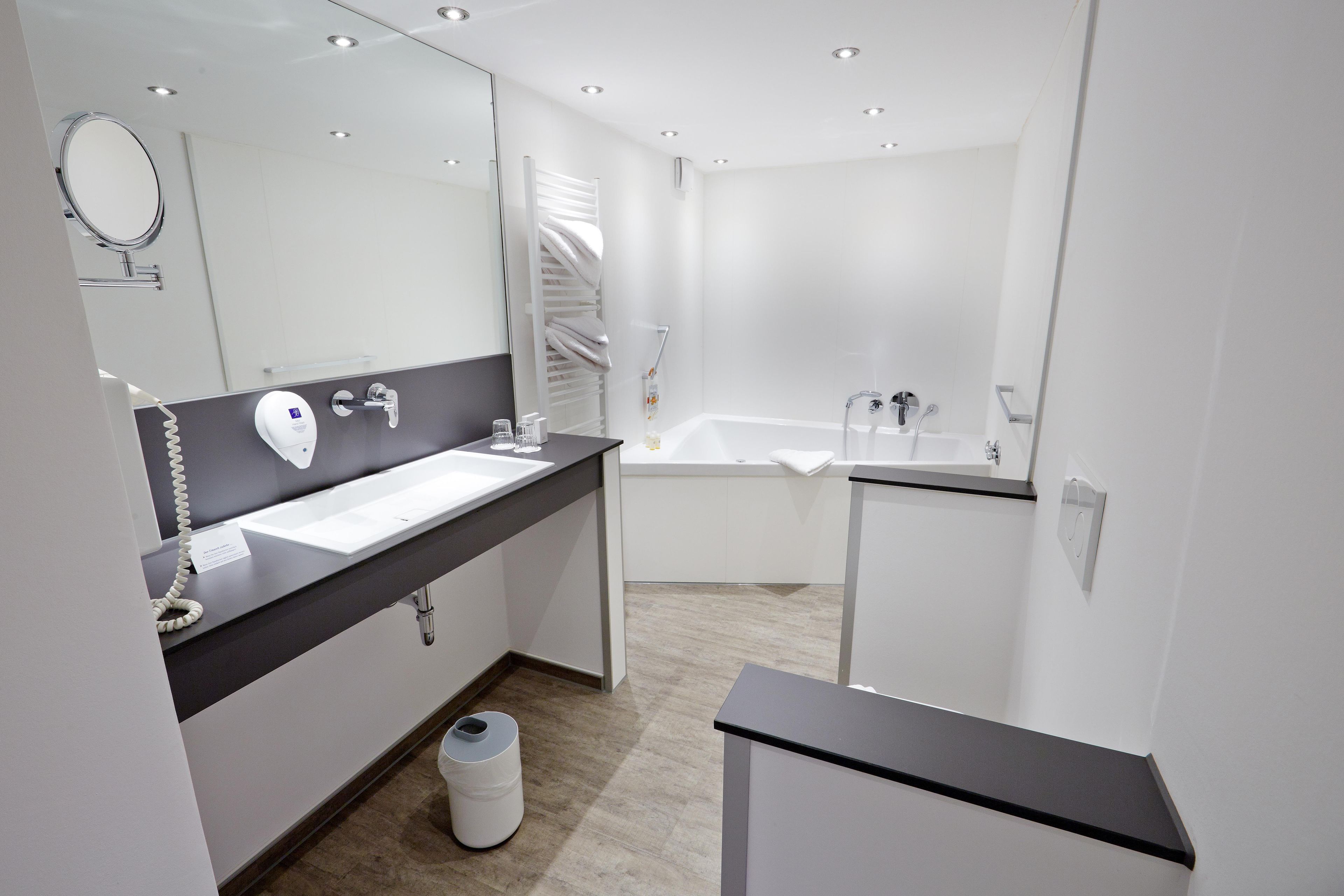 A modern bathroom with a large mirror, a sink, a bathtub, and a toilet.