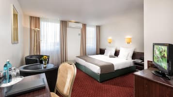 A hotel room with a bed, a desk, a chair, a television, and a window with curtains.
