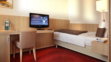 A hotel room with a bed, a desk, a chair, a TV, a lamp, and a phone.