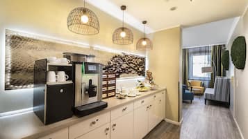 Eine kompakte Küchenzeile mit Kaffeemaschine, kleinem Kühlschrank und einer Kaffeestation mit Tassen und Tablett.