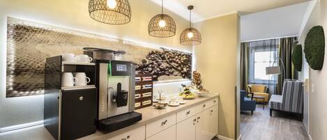 A compact kitchenette with a coffee machine, a small refrigerator, and a coffee station with cups and a tray.