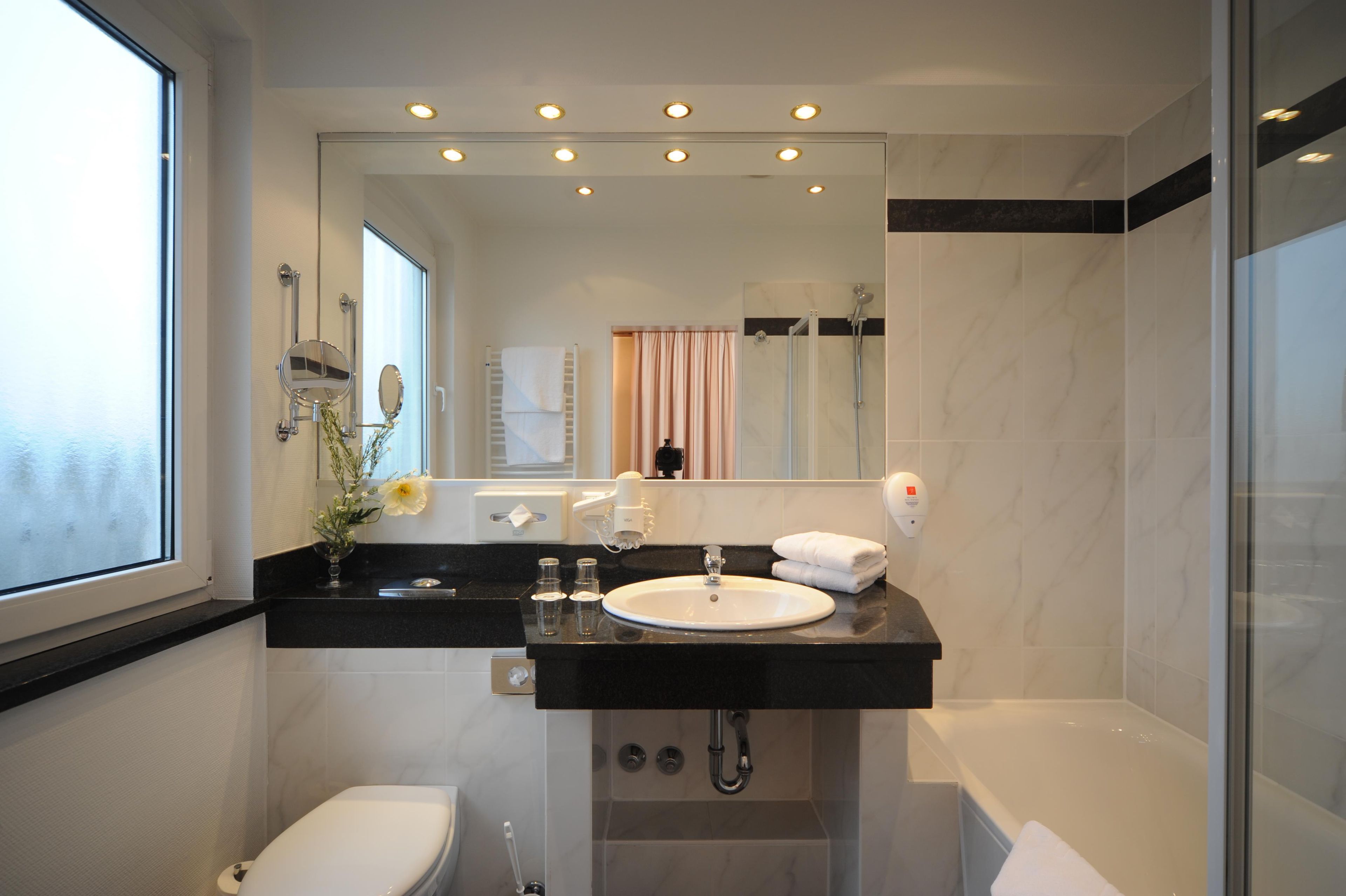 Un baño moderno con encimera negra, lavamanos blanco y ducha con cerramiento de vidrio.
