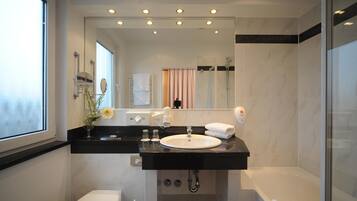 Un baño moderno con encimera negra, lavamanos blanco y ducha con cerramiento de vidrio.