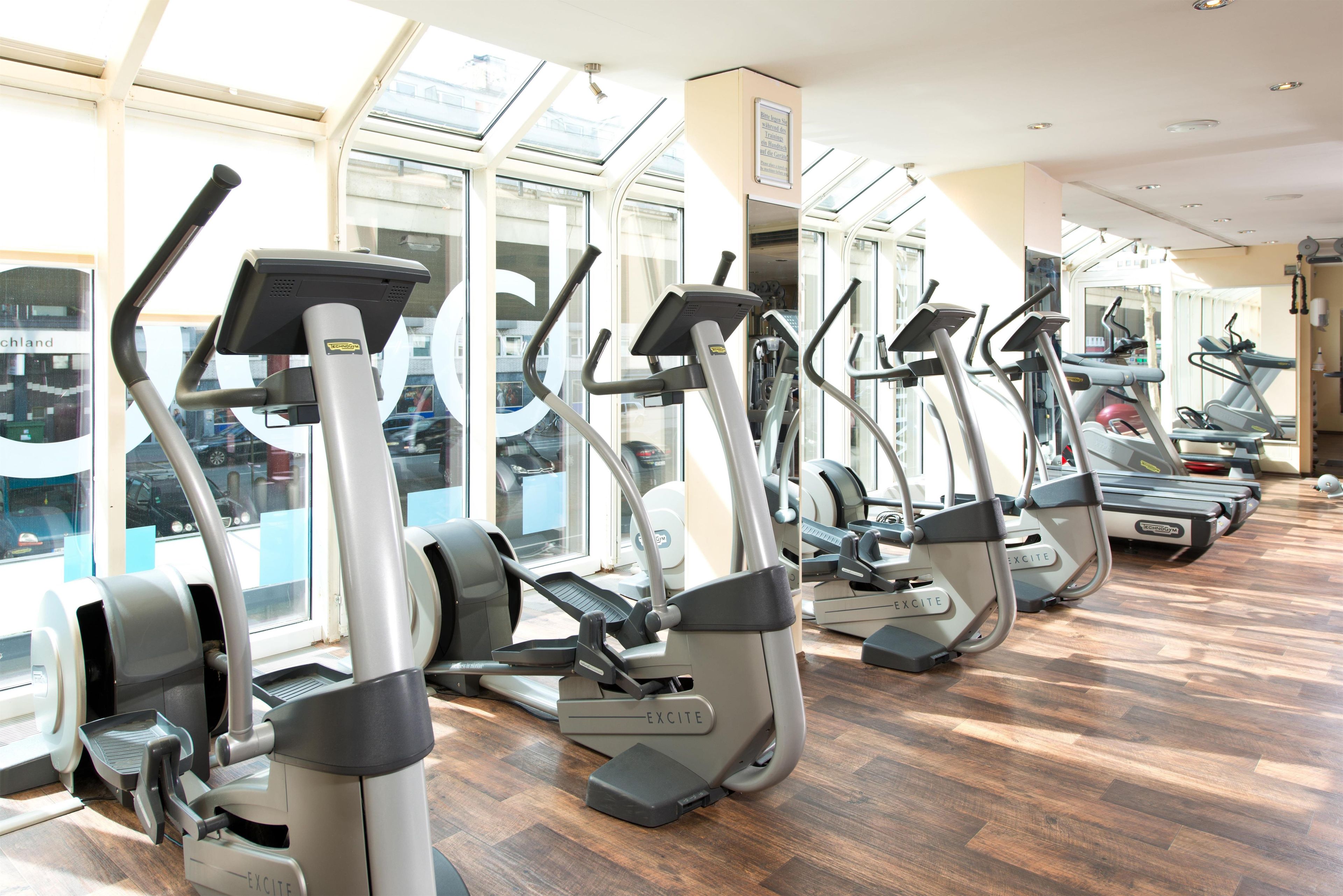 Eine Reihe von stehenden Ergometer in einem Fitnessstudio mit großen Fenstern und Holzboden.