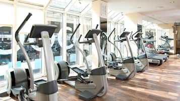 A row of stationary exercise bikes in a gym with large windows and a wooden floor.
