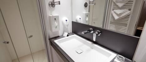 A modern bathroom with a white sink, a mirror, a towel rack, and a soap dispenser.