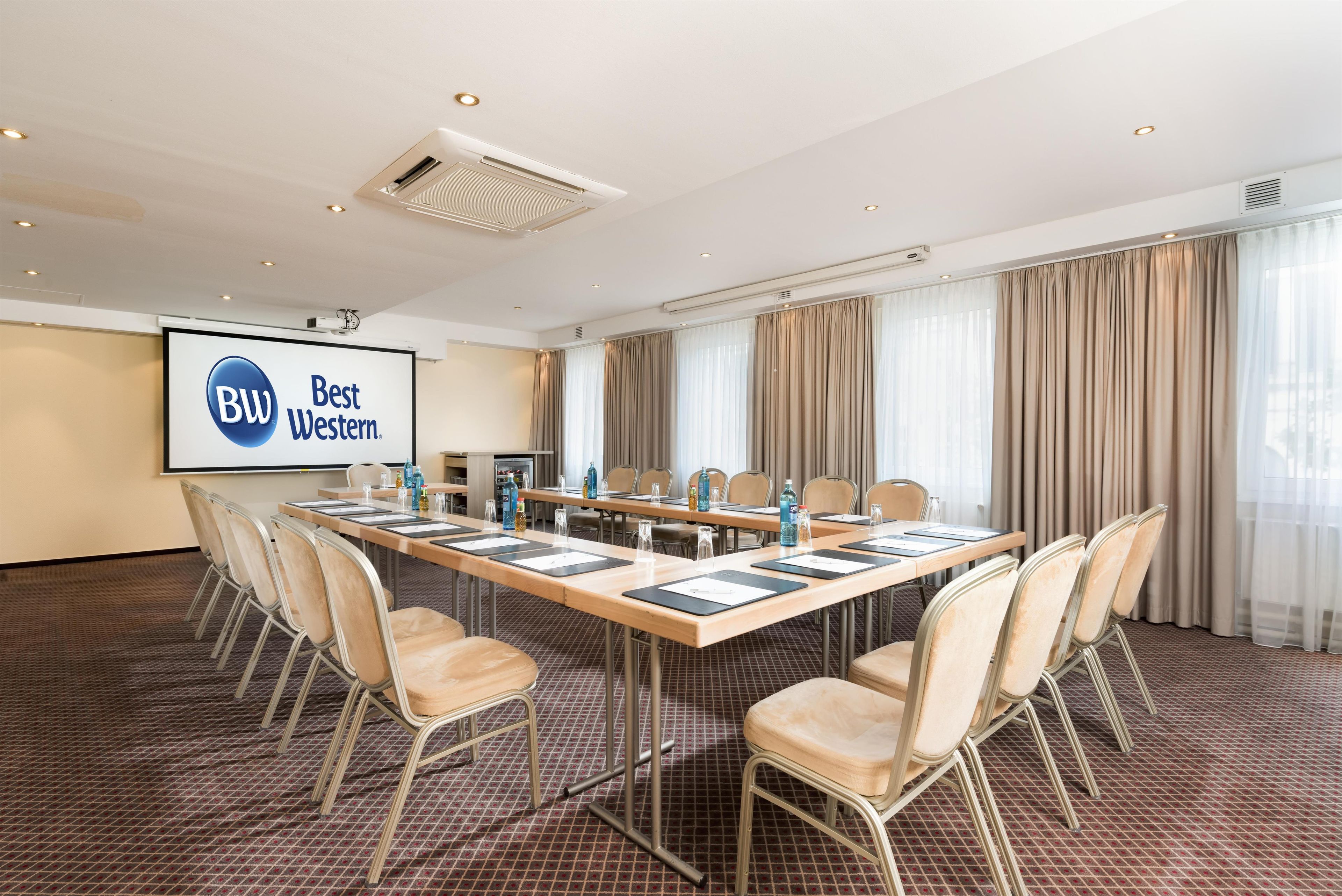 A conference room with a long table, chairs, a projector screen, and a large window with curtains.