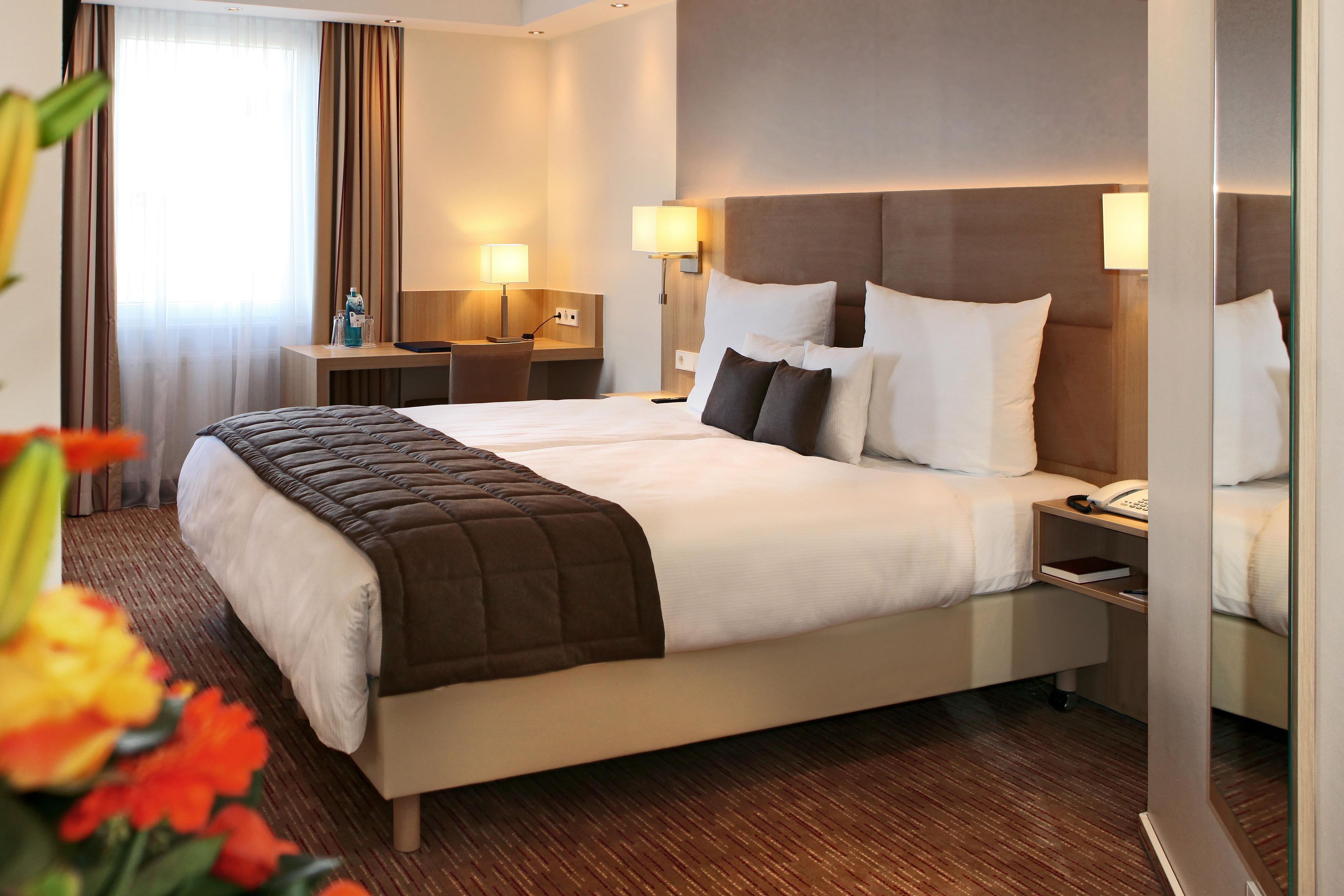 A hotel room with a double bed, bedside tables, lamps, a desk, and a chair.