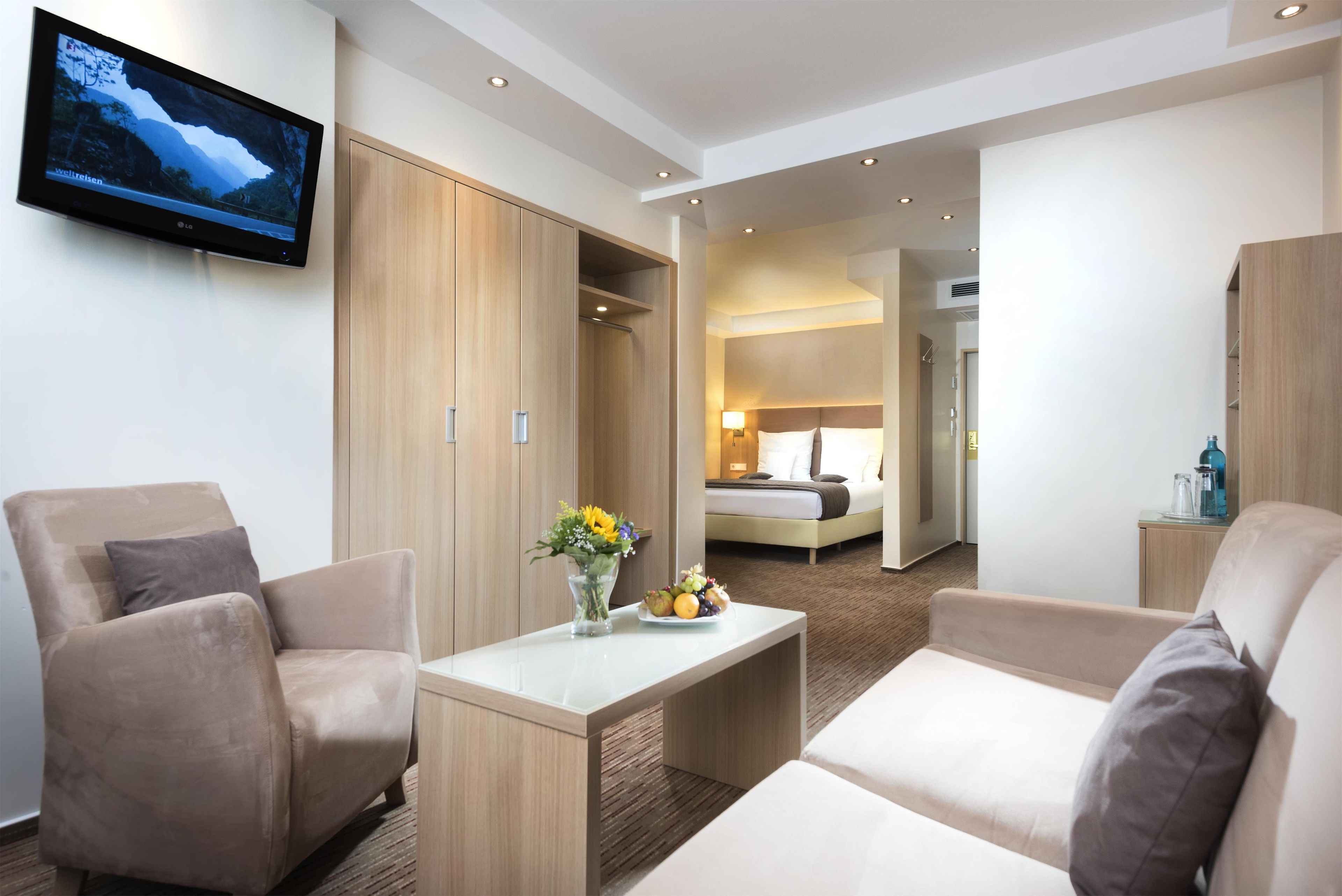 Ein Hotelzimmer mit Fernseher, Schreibtisch mit Blumenvase und Bett mit Nachttisch.