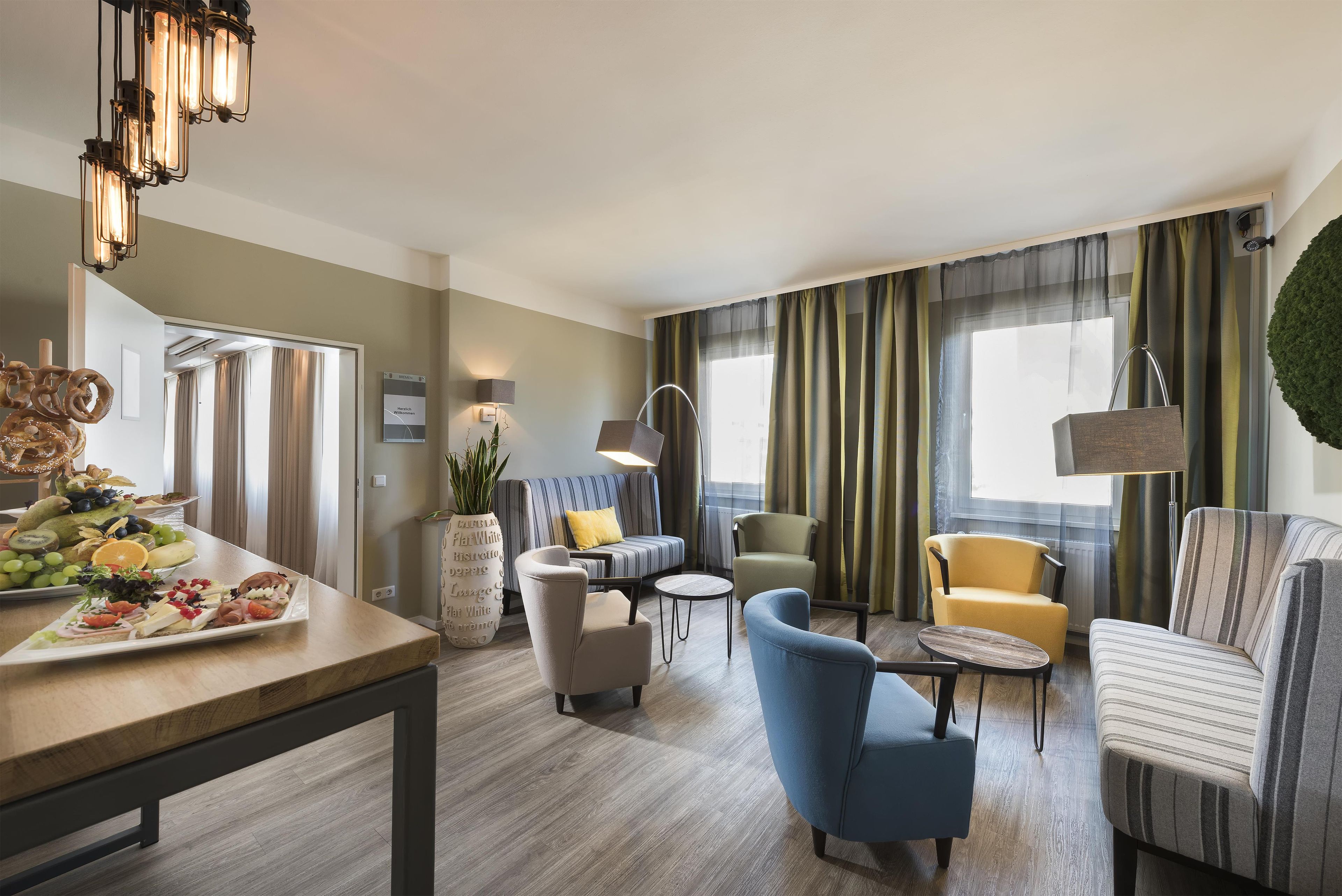 Ein modernes Wohnzimmer mit Essbereich, ausgestattet mit einer Couch, Sesseln, einem Couchtisch und einer Chandelüster.