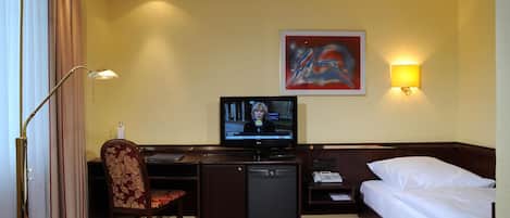 Una habitación de hotel con cama, escritorio, silla, televisor y un cuadro en la pared.