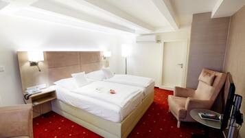 A hotel room with a bed, bedside table, lamp, chair, and a small table with a remote control.