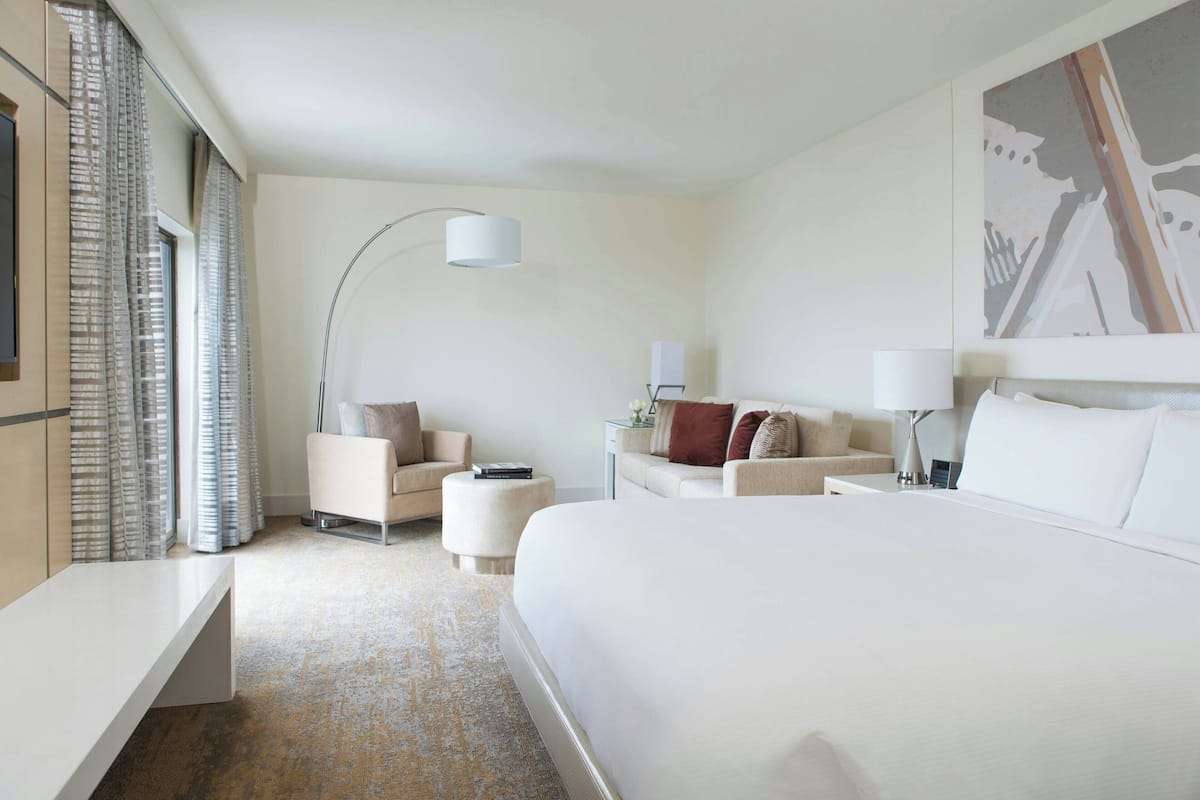 Habitación de hotel con una cama grande, dos sofás, un escritorio, una lámpara y un cuadro en la pared.