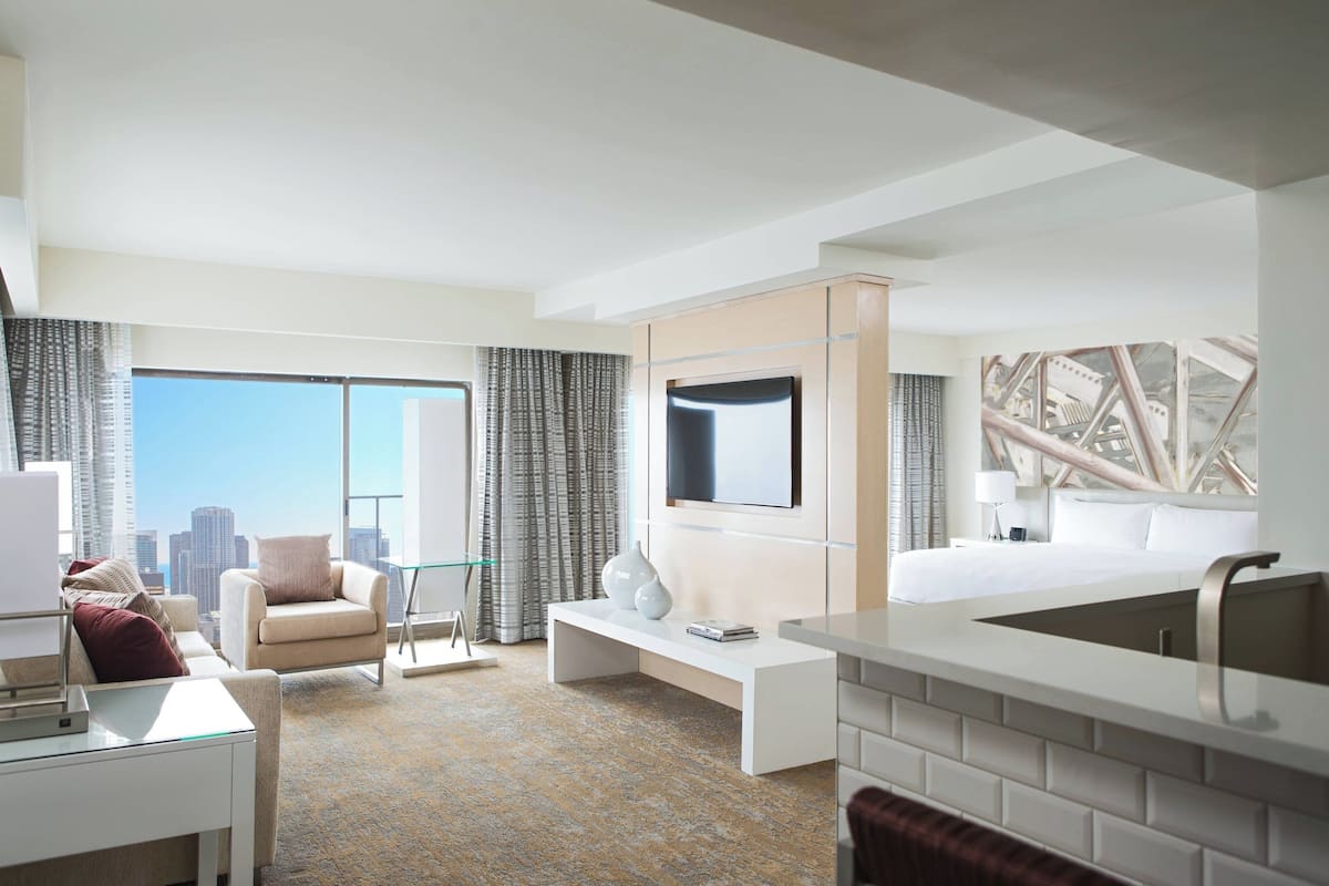 Una habitación de hotel moderna con una cama grande, un escritorio, una silla y vistas al horizonte de la ciudad.