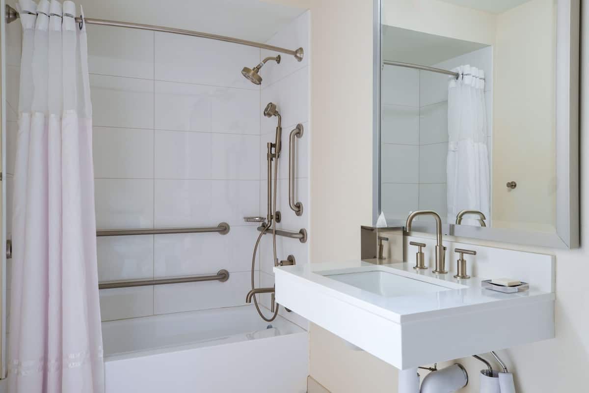 Un baño con una bañera blanca, un lavamanos con espejo y una ducha con barras de apoyo.