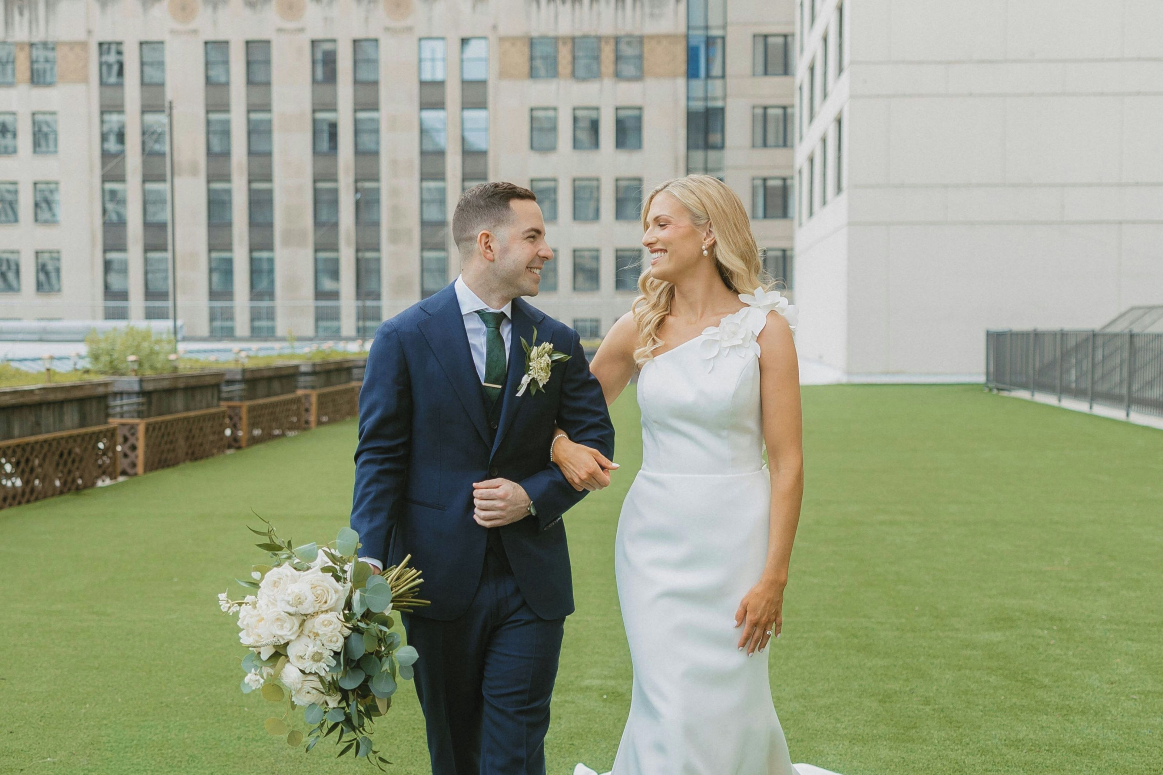 A couple holding hands on a grassy area with a building in the background.