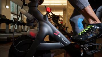 Uma bicicleta ergométrica Peloton com guidão vermelho, pedais pretos e banco preto.