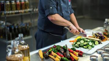 Un chef prépare des plats à base de légumes et de sauces sur un plan de travail en acier inoxydable.