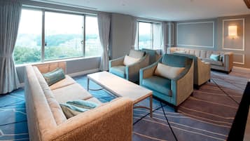 A modern hotel room with a large window, a sofa, two armchairs, a coffee table, and a patterned carpet.