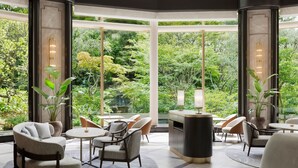 A modern hotel lobby with a large glass window offering a view of a lush garden. There are several seating areas with tables and chairs. - The Westin Tokyo (Tokyo)