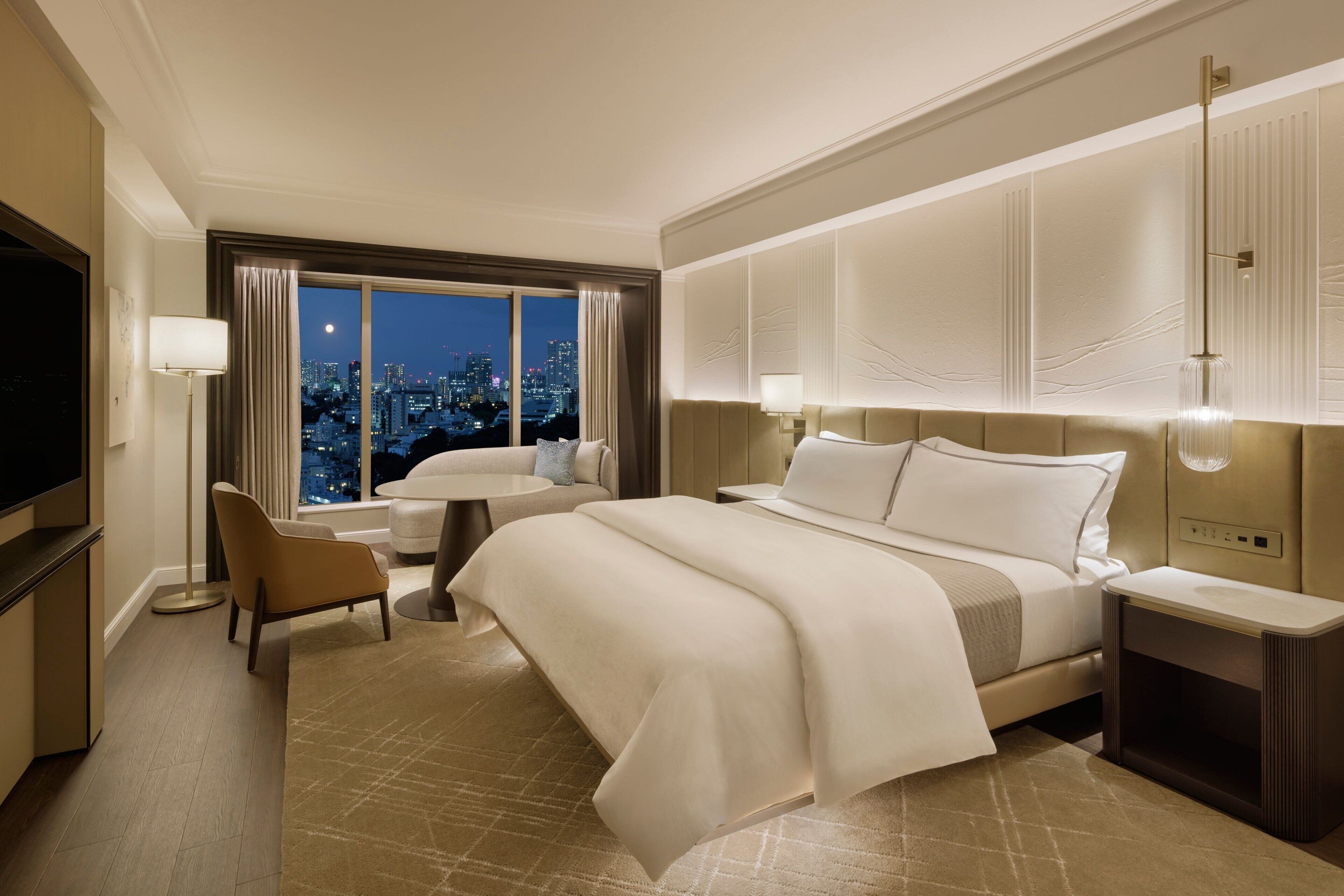Une chambre d’hôtel avec un grand lit, une télévision, un bureau et une vue sur la ville la nuit.