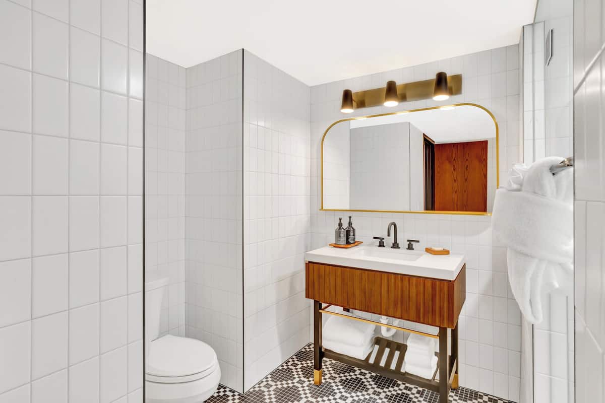 Ein modernes Badezimmer mit weißen Fliesen, einem Holz-Waschtisch, einer weißen Toilette und einer Duschkabine.