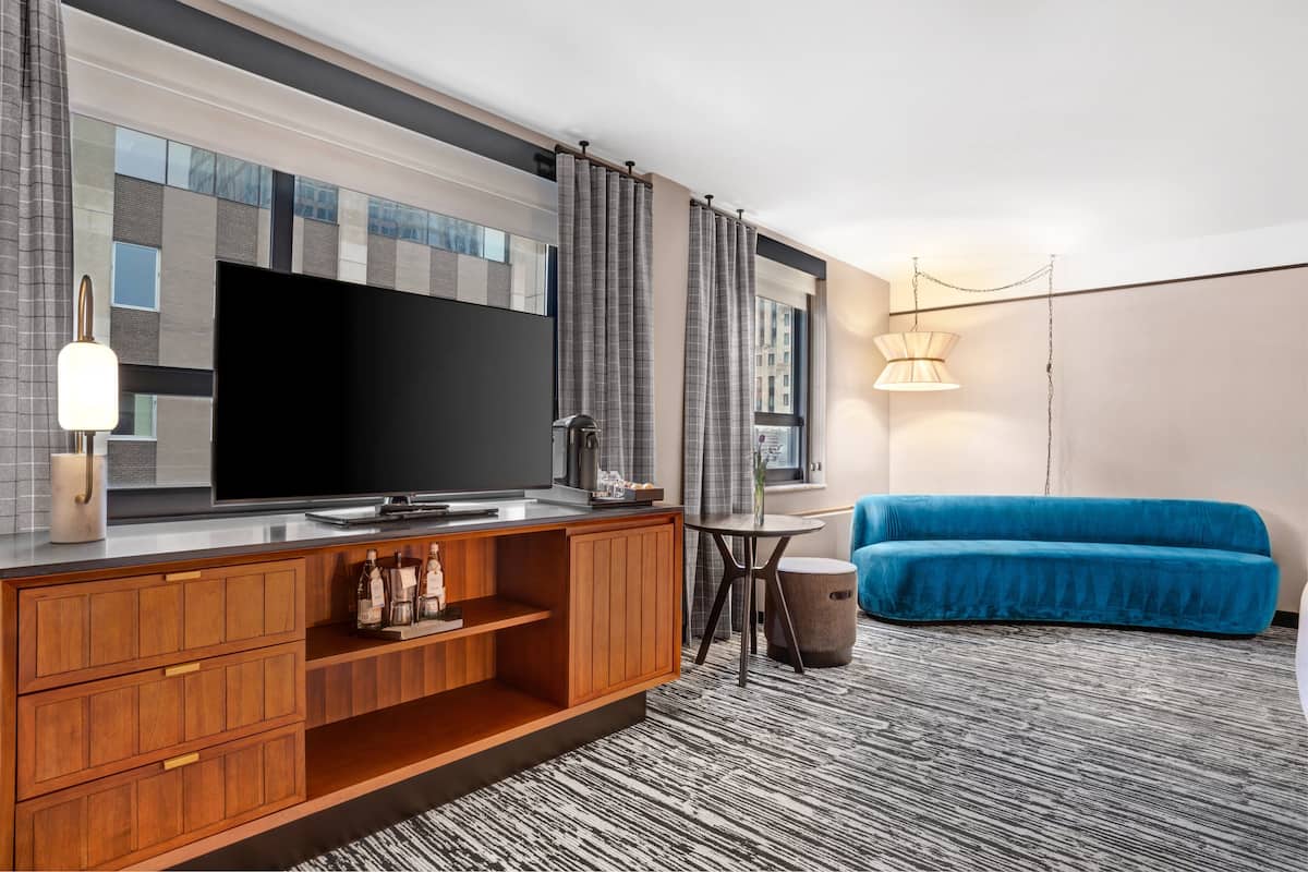 Ein modernes Hotelzimmer mit großem Flachbildfernseher, Holzkasten und blauem Sofa.