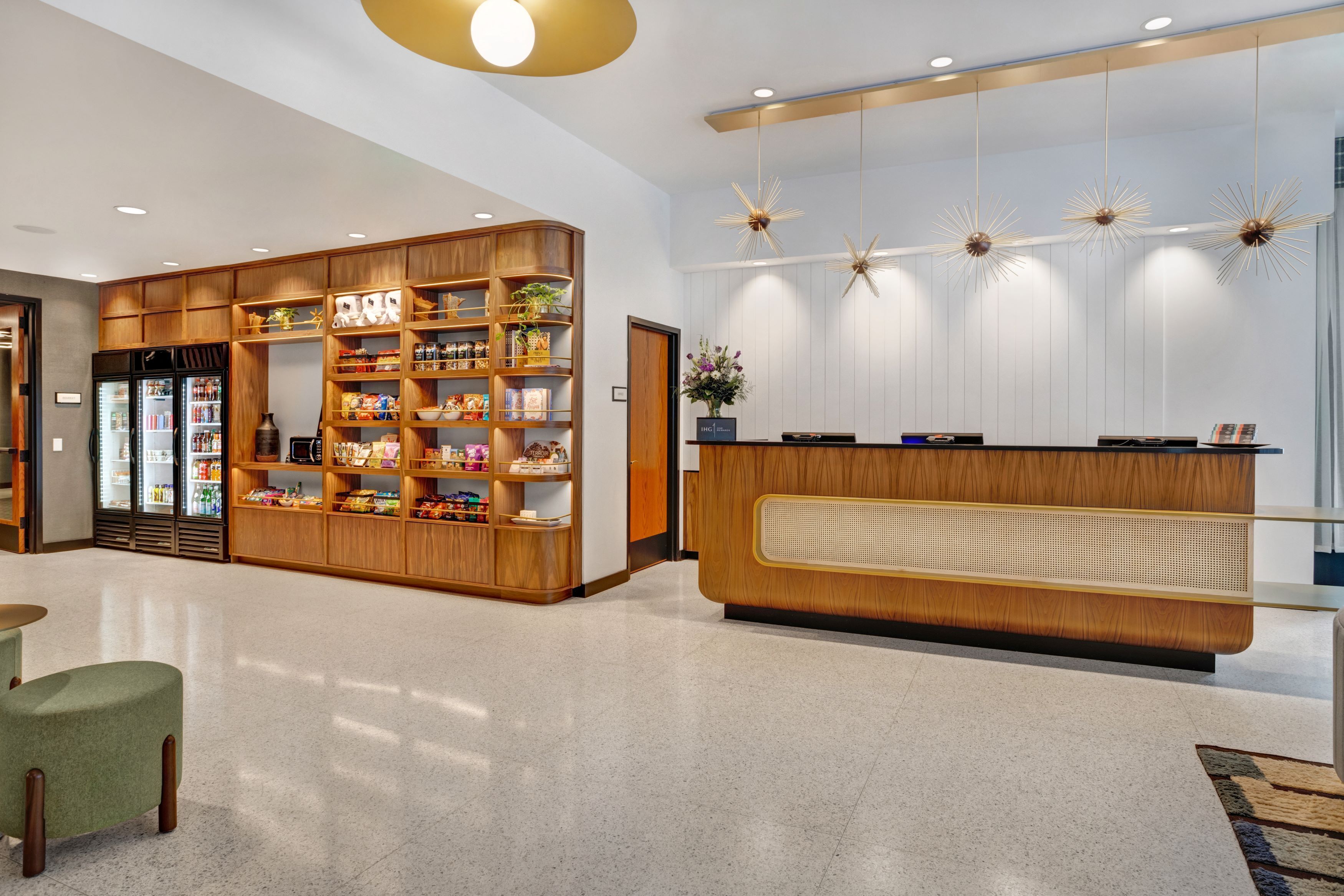 A modern reception area with a wooden reception desk, a large shelving unit with snacks and beverages, and decorative star-shaped pendant lights.