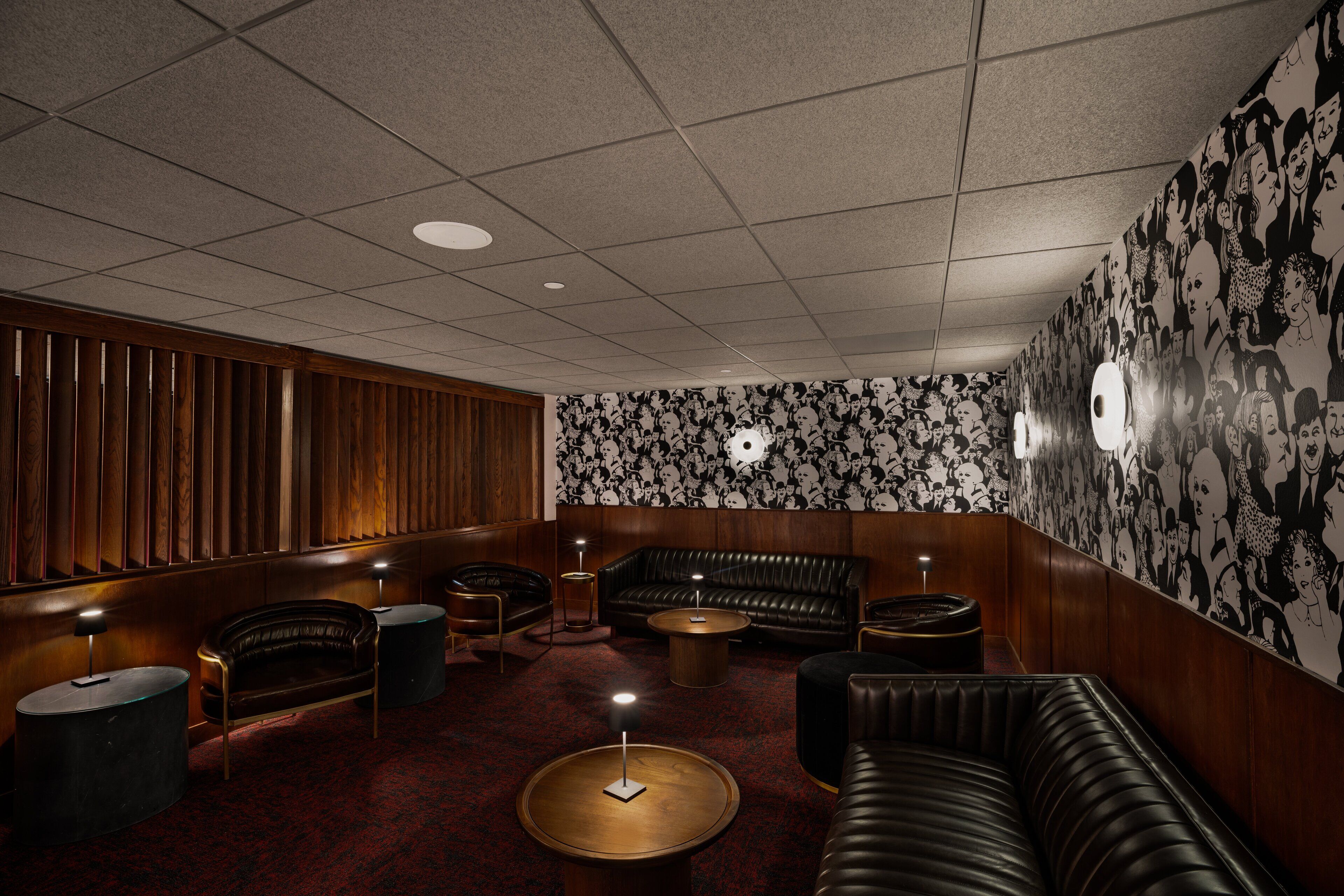 A lounge area with a patterned wall, leather sofas, and round tables.
