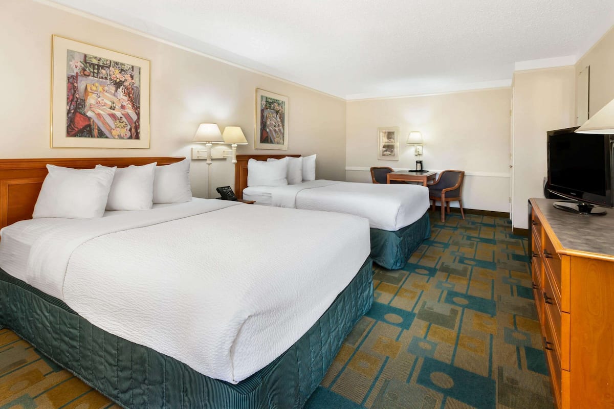 A hotel room with two beds, a desk, a chair, a television, and artwork on the walls.