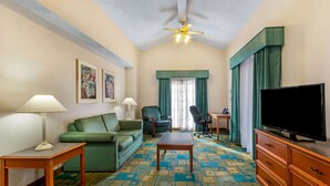 A hotel room with a green sofa, a wooden table, a TV on a wooden cabinet, and a patterned carpet. - La Quinta Inn by Wyndham Albuquerque Northeast (Albuquerque)