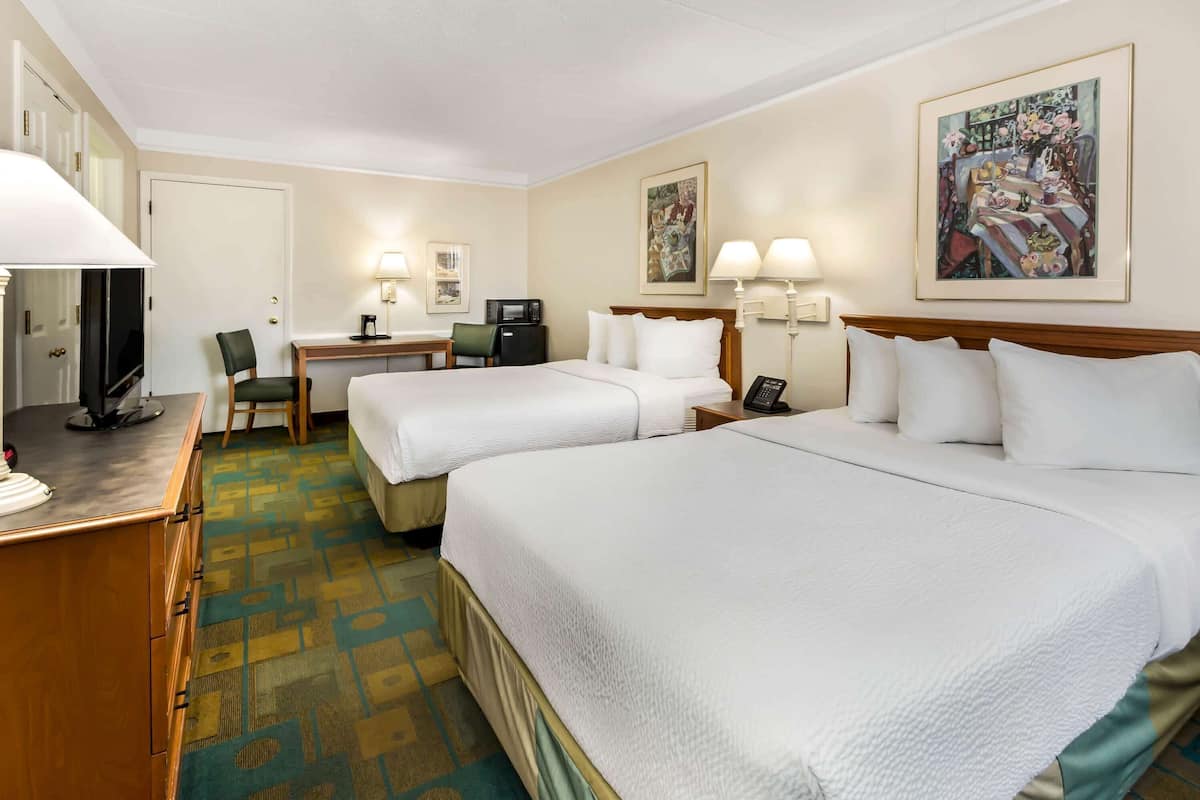 A hotel room with two beds, a desk, a chair, a television, and artwork on the walls.