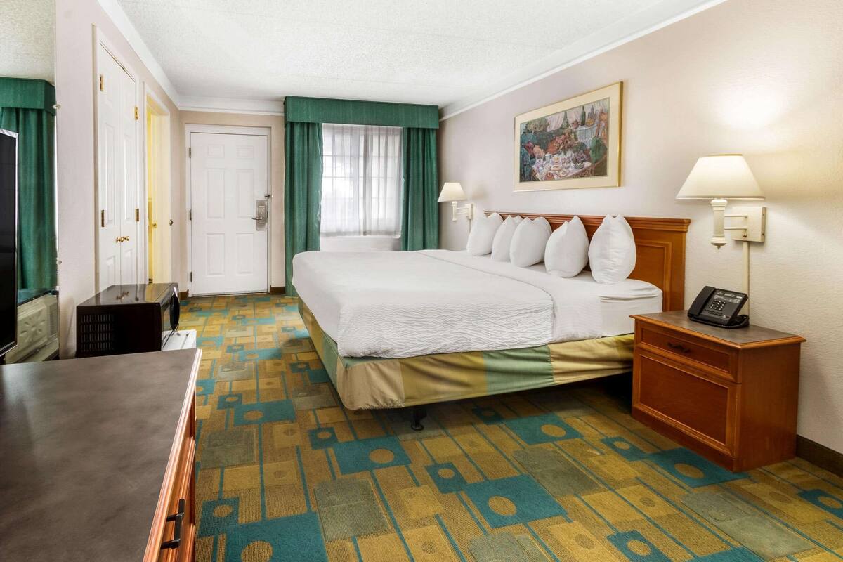 A hotel room with a bed, bedside table, lamp, and a painting on the wall.