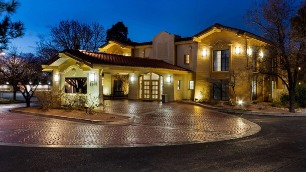A large, well-lit building with a prominent entrance, paved driveway, and surrounding trees. - La Quinta Inn by Wyndham Albuquerque Northeast (Albuquerque)