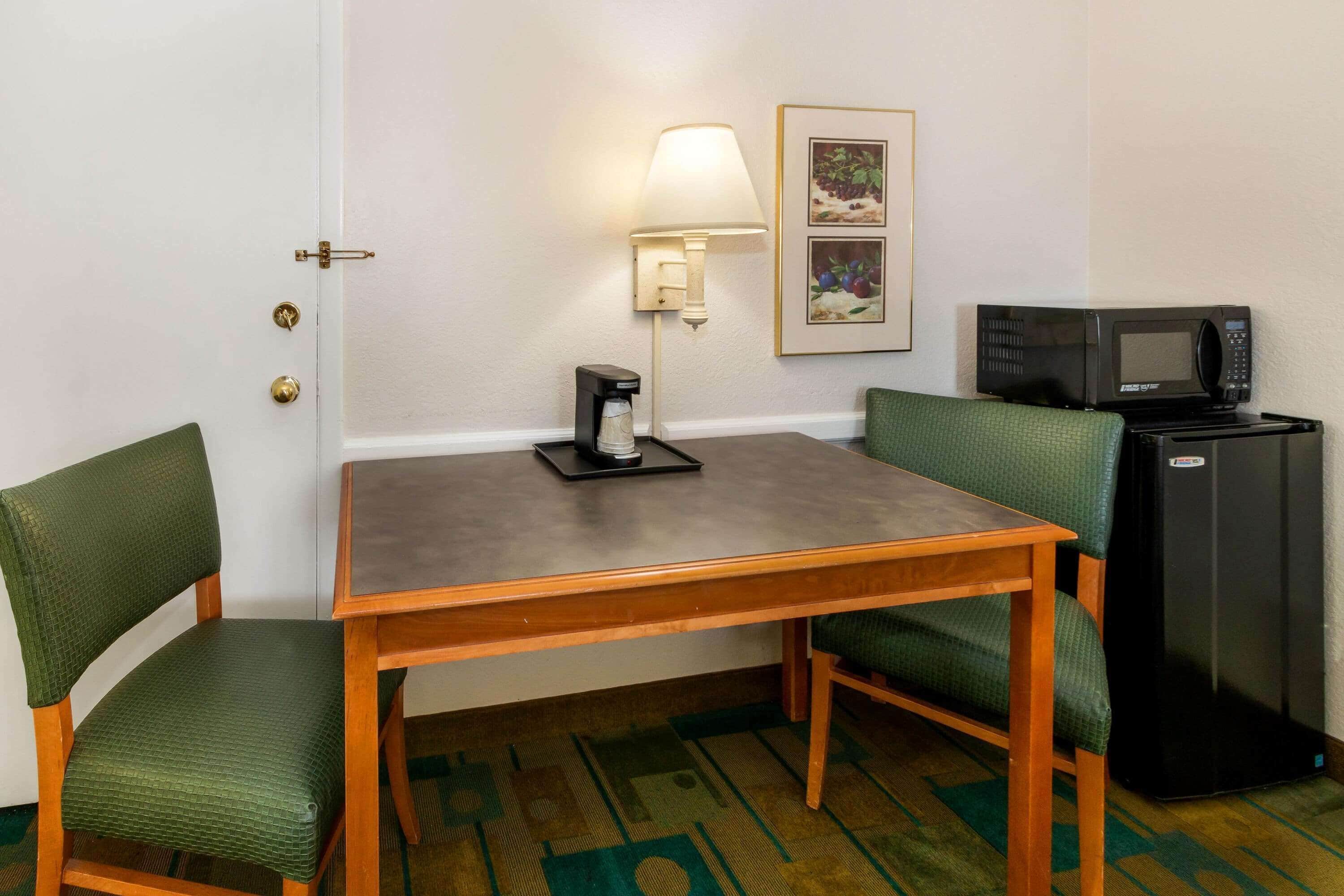 Une petite pièce avec une table en bois, deux chaises vertes à coussins, une machine à café, un four à micro-ondes et un réfrigérateur.