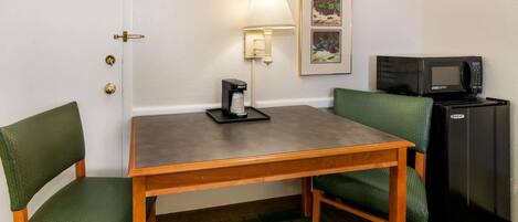 A small room with a wooden table, two green cushioned chairs, a coffee maker, a microwave, and a refrigerator.