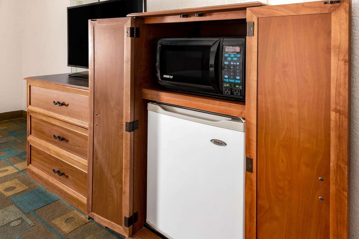 A compact kitchenette with a microwave, a small refrigerator, and a wooden cabinet with drawers.