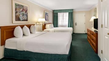 A hotel room with two beds, a wooden headboard, a desk with a lamp, a television, and artwork on the walls.