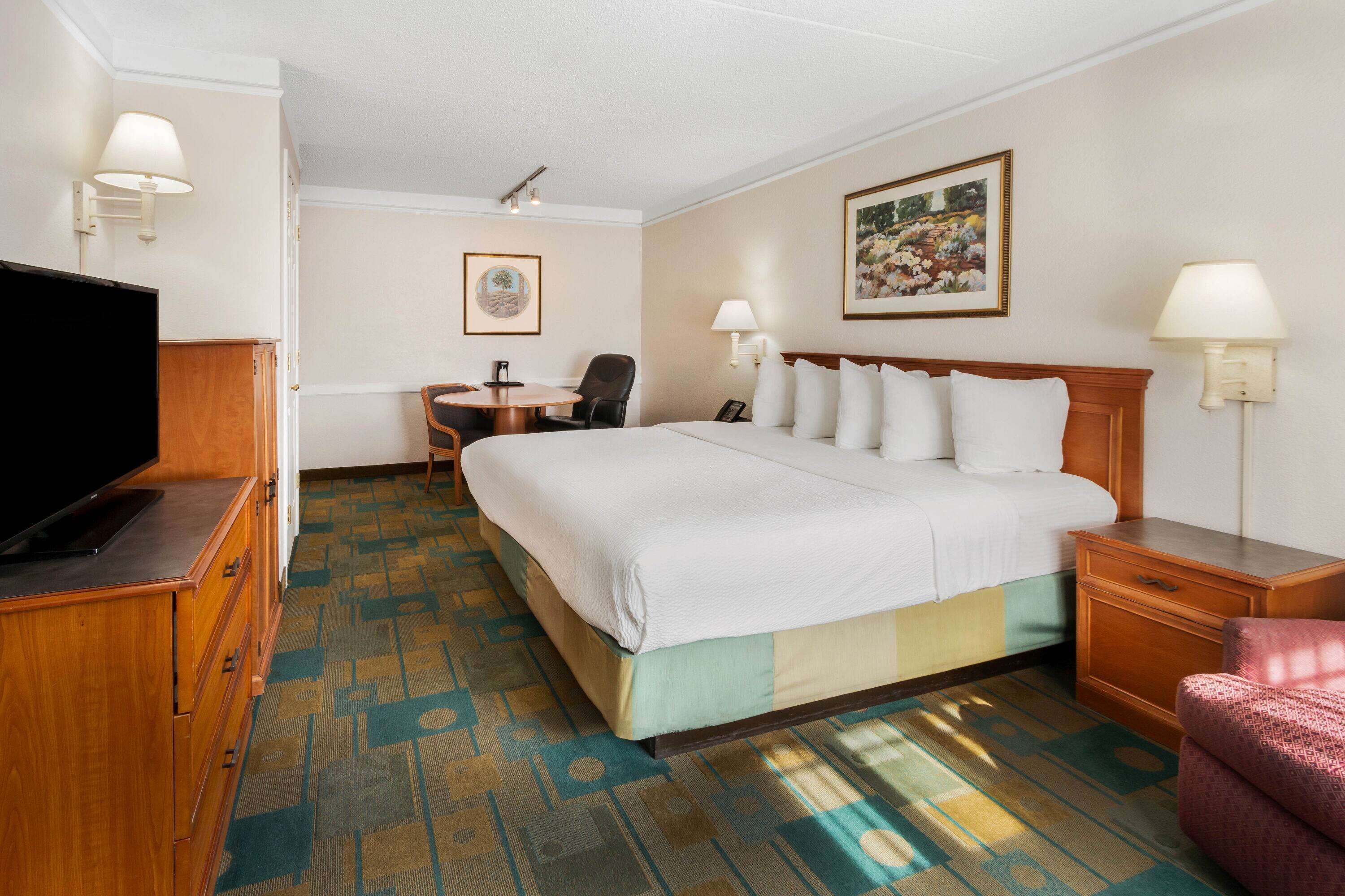 A hotel room with a large bed, a desk with a chair, a television, and a lamp.