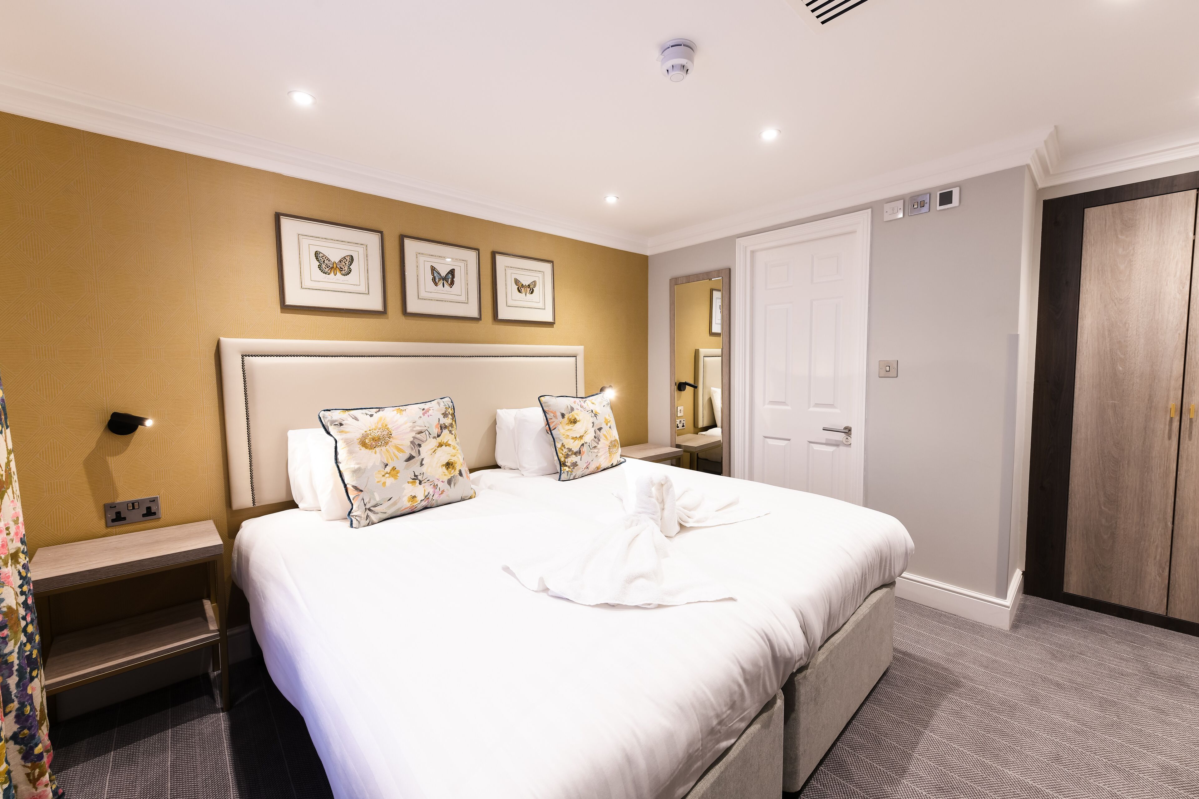 A hotel room with a large bed, a bedside table, a wardrobe, and a mirror.